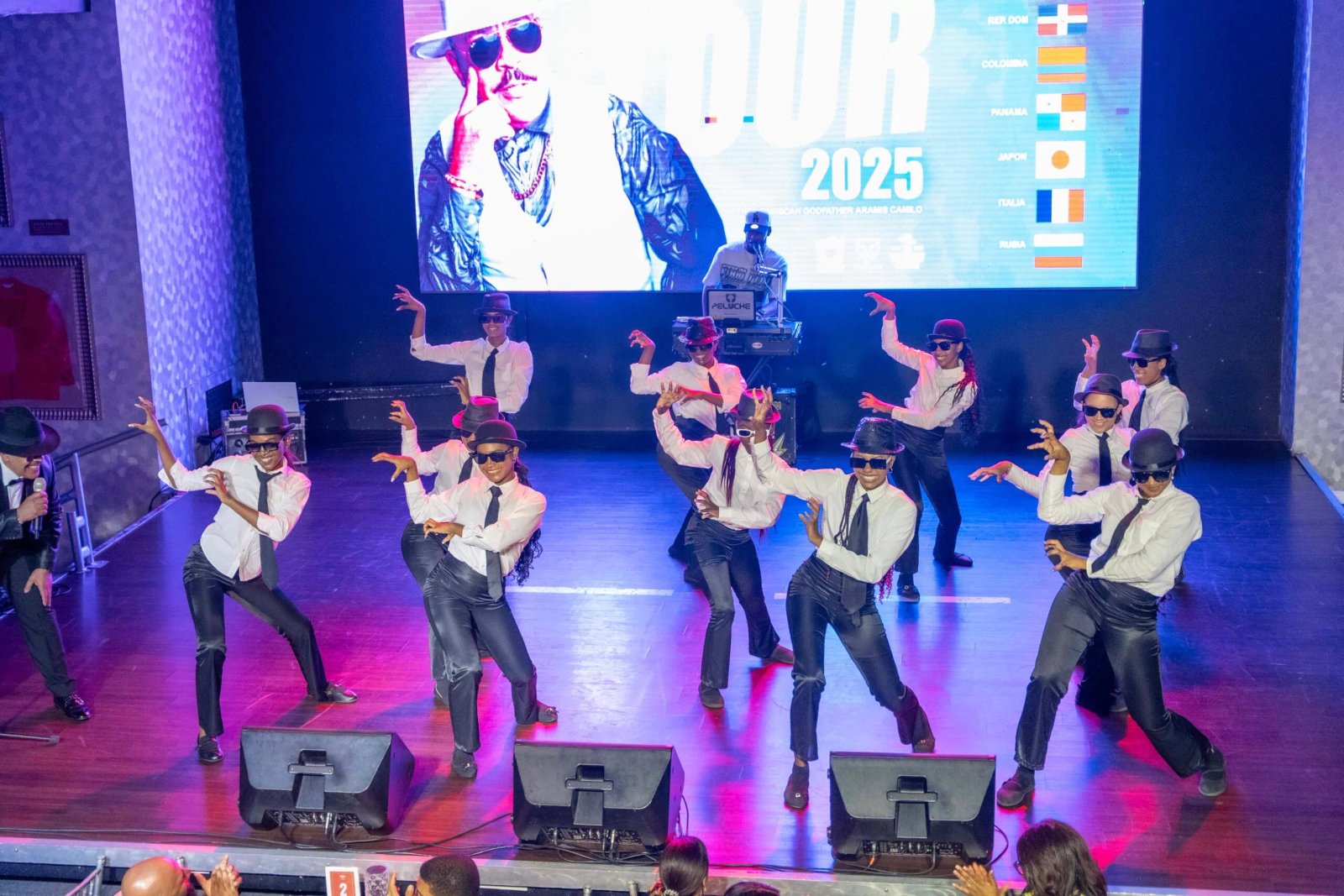 Grupo de bailarines actuando en escenario con pantalla grande.